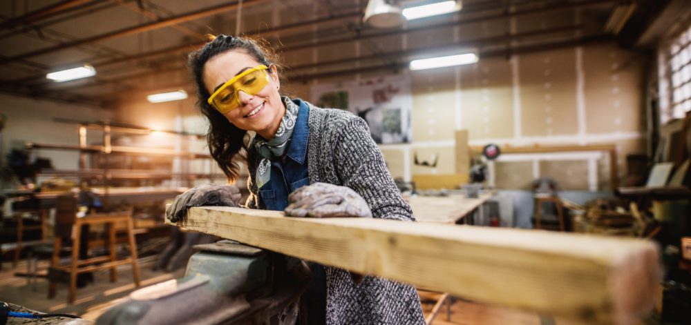 Professional carpenter woman choosing and preparing wood at steel vise in the fabric workshop.