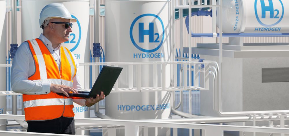 Man works for energy company. Engineer stands among hydrogen equipment. Mechanic with laptop controls process of obtaining energy. Man inspects hydrogen power plant. Getting electricity from hydrogen H2